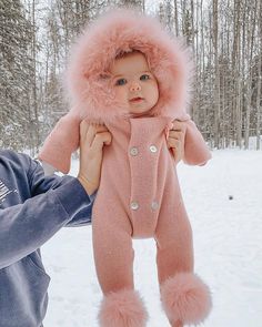 a man holding a baby in the snow wearing a pink winter suit and fur hat