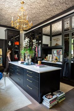 a woman is walking through a room with black cabinets and gold trimmings on the ceiling