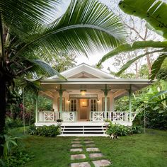 a small white house surrounded by lush green trees and bushes with steps leading up to the front door