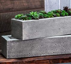 two concrete planters with succulent plants in them sitting on a table outside