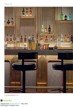 two bar stools in front of a gold wall with liquor bottles on the shelves