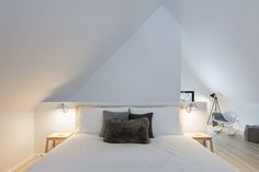 a bed with white sheets and pillows in a room that has slanted ceiling lights