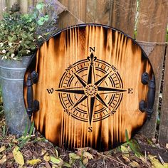 a wooden sign with a compass on it sitting next to a potted plant and fence