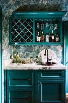 a kitchen with green cabinets and marble counter tops, wine bottles on the shelves above the sink