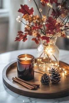 a candle and some cinnamon sticks on a tray with christmas lights in the back ground