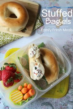 two plastic containers filled with food next to strawberries and bagels on a table