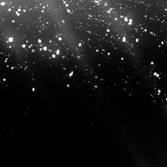 black and white photograph of snow flakes in the night sky with sunbeams