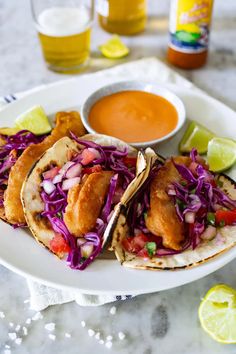 three fish tacos with coleslaw and salsa on a white plate next to a bowl of dipping sauce