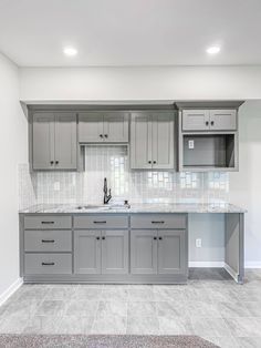 an empty kitchen with gray cabinets and marble counter tops in the middle of the room