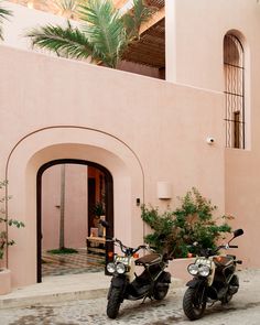 two motorcycles parked next to each other in front of a pink building with palm trees