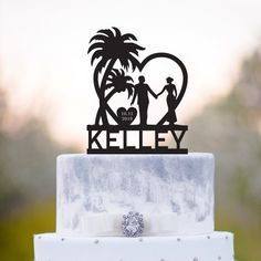 a wedding cake topper with a couple holding hands and palm trees in the background