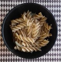 a black bowl filled with pasta on top of a checkered tablecloth covered floor