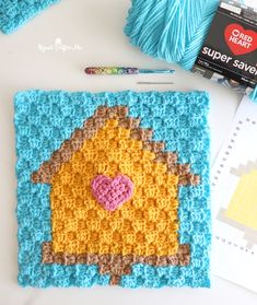 a crocheted house with a heart on it next to some yarn and scissors