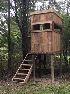 a wooden tree house with stairs in the woods next to it and trees behind it