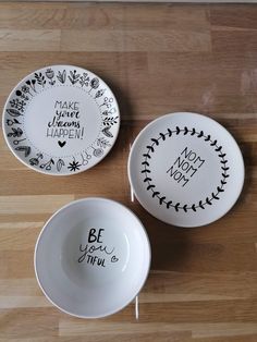 three white bowls with black lettering on them sitting on a wooden floor next to each other