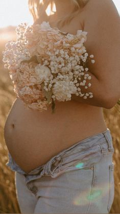 a pregnant woman with flowers in her belly is standing in the middle of a field