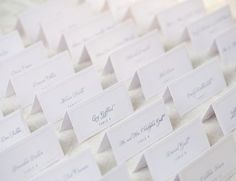 there are many place cards on top of the white table cloth, which is lined up in rows