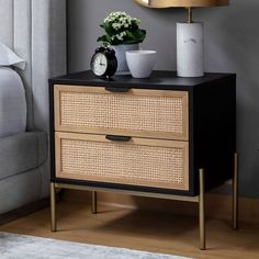 a nightstand with two drawers and a clock on it next to a bed in a bedroom