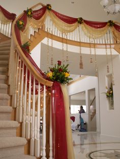 a staircase decorated with red and gold ribbons, garlands and flowers on the railing