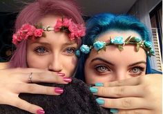 two women with blue and pink hair are posing for the camera, both wearing flower crowns