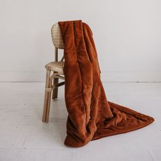 a brown blanket sitting on top of a chair next to a wooden chair with a white wall in the background