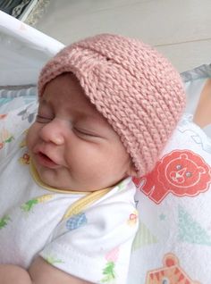 a baby wearing a pink knitted hat laying on top of a white blanket in a crib