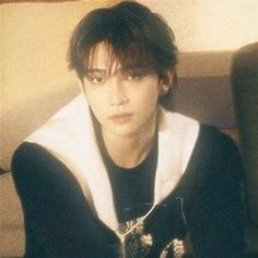 a young man sitting on top of a couch wearing a black and white shirt with hoodie over his shoulders