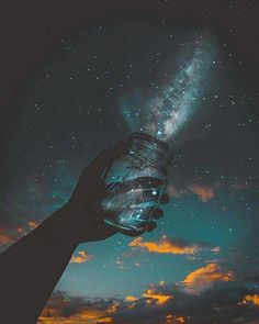 a hand holding a jar filled with water under a night sky full of stars and clouds