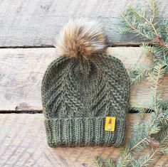 a knitted hat with a fur pom sits on top of a wooden table