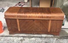 a wooden chest sitting on top of a sidewalk next to an orange bucket and other items