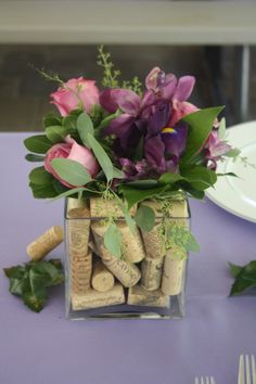 a vase filled with flowers and wine corks on top of a purple table cloth