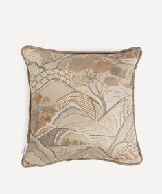 an embroidered pillow with trees and mountains on the back in beige, brown and white