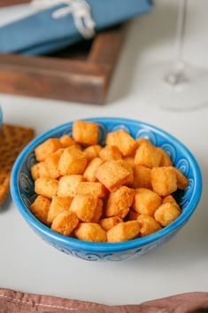 a blue bowl filled with tater tots on top of a table next to a glass of wine