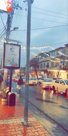 a city street with cars and people walking on the side walk at night, in the rain