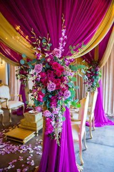 a purple and yellow wedding arch with flowers on the side, draped over by draping