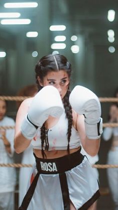 a woman wearing boxing gloves standing in front of a rope with her hands on her hips