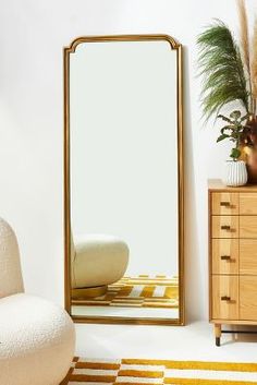 a mirror sitting on top of a wooden dresser next to a white chair and potted plant