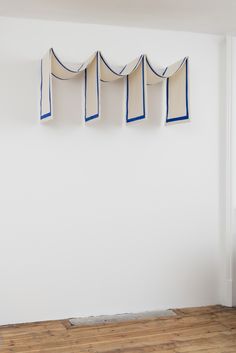 an empty room with four blue and white objects hanging on the wall, in front of a wooden floor