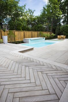 an outdoor swimming pool surrounded by wooden fence and shrubbery on the other side, with benches in the foreground