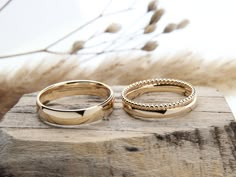 two gold wedding rings sitting on top of a piece of wood next to each other