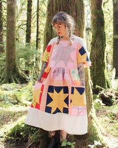 a woman standing next to a tree wearing a dress made from patchwork fabric and leather boots