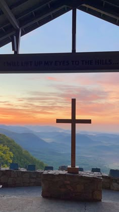 a wooden cross sitting on top of a stone slab under a roof with a sunset in the background