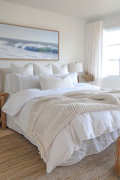 a bed with white linens and blankets in a bedroom next to a painting on the wall