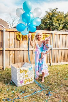 a woman holding a baby in her arms while standing next to a box with balloons