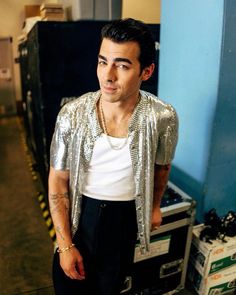 a man standing in front of a stack of boxes wearing a silver jacket and white t - shirt