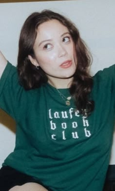 a woman sitting on top of a bed wearing a green shirt