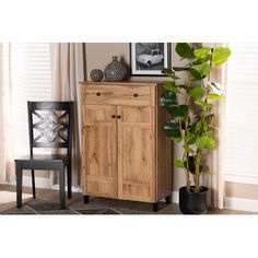 a wooden cabinet next to a black chair and potted plant in a living room