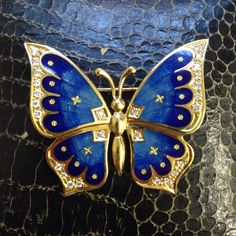 a blue and gold butterfly brooch sitting on top of a black snake skin surface