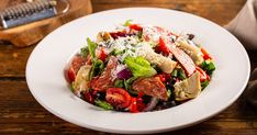 a salad with tomatoes, lettuce and other vegetables on a white plate sitting on a wooden table