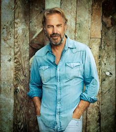 a man standing in front of a wooden wall with his hands in his pockets and looking at the camera